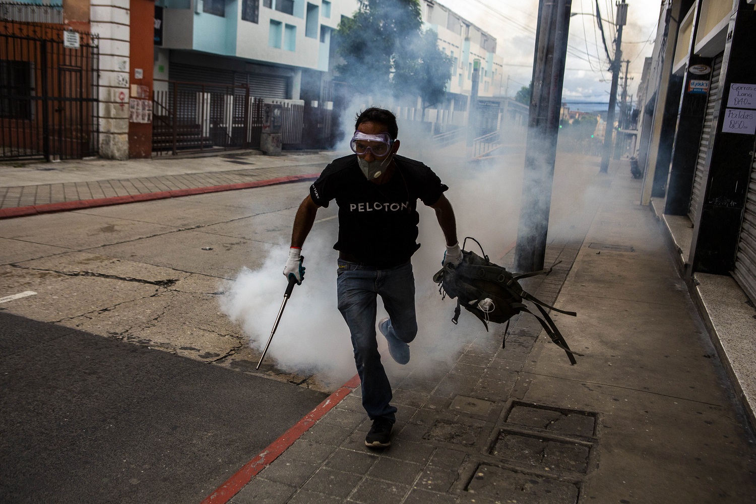 Un manifestante protegido con lentes protectores y cargando un bastón en la mano escapa de una bomba lacrimógena lanzada por la policía durante la manifestación del 21 de noviembre del 2020. | Foto: Oliver de Ros